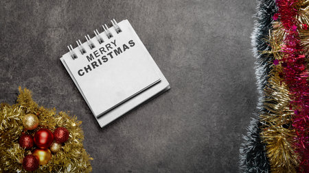 Greeting of Merry Christmas text in a notepad on a black background. Mockup or Copy space. Holiday greetings or winter themes. Concept of the Merry Christmas celebrationの写真素材