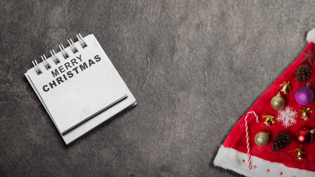 Greeting of Merry Christmas text in a notepad on a black background. Mockup or Copy space. Holiday greetings or winter themes. Concept of the Merry Christmas celebrationの写真素材