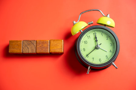 Green alarm clock with row of wooden cubes on colored background. Empty area for copy space. Concept of time, reminder, or deadlineの写真素材