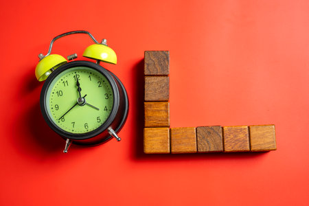 Green alarm clock with row of wooden cubes on colored background. Empty area for copy space. Concept of time, reminder, or deadlineの写真素材