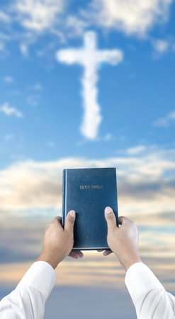 Prayer holding the blue book of the holy bible with light of the Christian cross on blue sky background. Concept of Christianity, religious, faith, Jesus, or beliefの写真素材