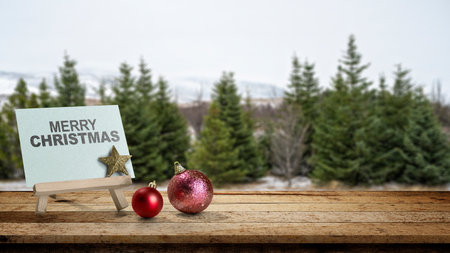 Greeting card of Merry Christmas with Christmas ornaments on the table with a snowy field background. Holiday greetings or winter themes. Concept of the Merry Christmas celebrationの写真素材