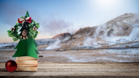 Paper Christmas tree with a wreath, bells, and bow. Wooden blocks with a Christmas ornament on the table. Copy space. Holiday greetings or winter themes. Concept of the Merry Christmas celebrationの写真素材