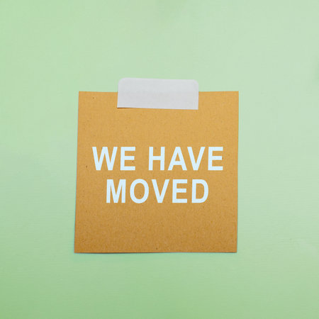 Square cardboard card with the white text "WE HAVE MOVED" on a light green background, emphasizing a change of address or relocation announcement conceptの写真素材