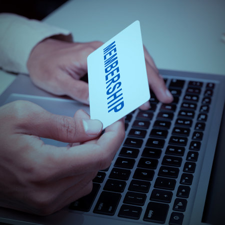 Business hand holding a membership card in their hand, over a laptop keyboard. The scene suggests...