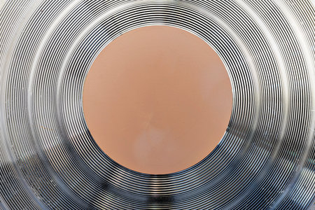 Macro shot of the bottom of a professional cookware pan showing metallic concentric ridges for even heat distribution and a central orange core. Industrial and abstract backgroundの写真素材