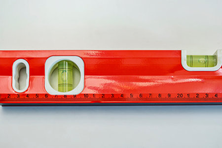 A close-up shot of a professional red spirit level featuring bubble vials and a metric ruler scale,...