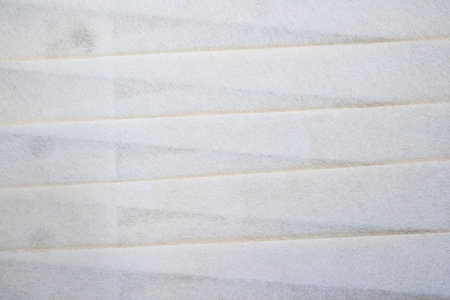 A macro shot of white pleated filter material showing its fibrous texture and diagonal folds....