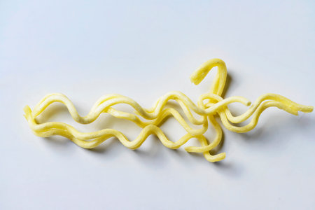 A detailed view of a few strands of yellow, wavy, uncooked instant noodles placed on a clean white...