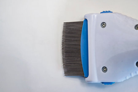 A close-up view of an electronic lice comb featuring fine metal teeth and a white plastic body, used...