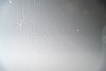A close-up view of a gray painted surface featuring vertical liquid streaks and drips, creating an industrial background for design projectsの写真素材
