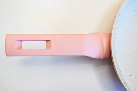 Close-up of a stylish pastel pink handle on a modern ceramic non-stick frying pan, isolated on a white background. Minimalist kitchenware design for contemporary cookingの写真素材