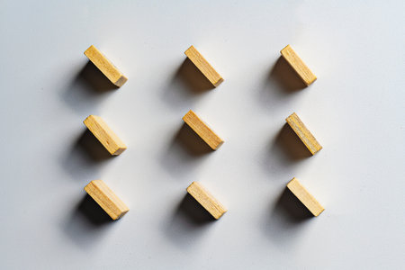 High-angle minimalist shot of nine wooden blocks neatly arranged in a 3x3 grid on a white background...