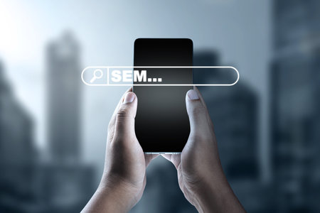 A close-up of hands holding a smartphone with an SEM search bar overlay, symbolizing digital marketing and search engine marketing optimization in a modern business environmentの写真素材
