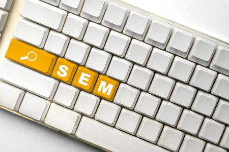 White computer keyboard featuring orange keys spelling out SEM with a search icon, illustrating digital marketing and search engine marketing strategiesの写真素材