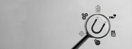 Minimalist banner of a magnifying glass over a magnet icon, surrounded by business symbols representing inbound marketing, customer attraction, and strategic growth on gray backgroundの写真素材