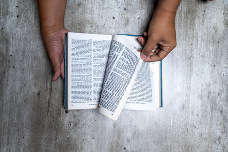 A top-down shot of a person's hands holding an open Bible on a textured gray surface, captured while...