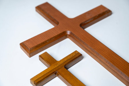 A high-angle shot of a large and a small wooden Christian cross resting on a clean white surface,...