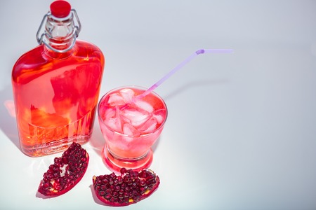 Pieces of an open Pomegranate showing the red arils with a Full bottle of fresh juice and a poured...