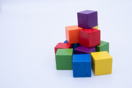 A haphazard pile of vibrant wooden toy blocks in various colors including red, blue, green, yellow, orange, and purple, against a white background.の写真素材