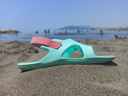 Lonely Sandal on the Beach: A Day at the Sea
A single light blue sandal with a pink strap sits abandoned on the dark sand of a beach, with a blurred ocean and people in the backgrの写真素材
