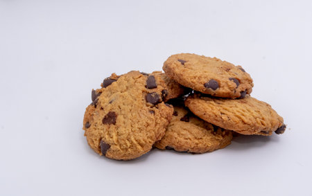 A tempting stack of freshly baked chocolate chip cookies, showcasing their golden color and rich chocolate pieces against a clean white backdrop.の写真素材