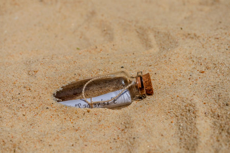 Glass bottle with a message inside emerging from the sand of a beach, concept of communication and discoveryの写真素材