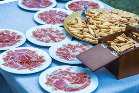Cured ham slices with crunchy breadsticks and crackers arranged on a table, offering a delicious appetizer spread for a social gatheringの写真素材