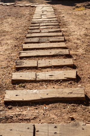 Rustic wooden planks forming a pathway or steps on dry dirt ground, representing progress, journey, and a natural trailの写真素材