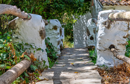Rustic stone path leading through a green garden, featuring whitewashed stone walls and natural wooden handrails on a sunny dayの写真素材