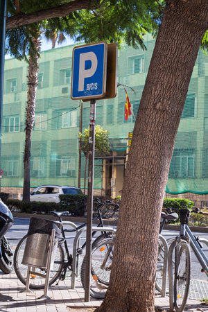 Blue parking sign for bicycles on a city street, with bikes parked at a rack, promoting sustainable urban transportationの写真素材