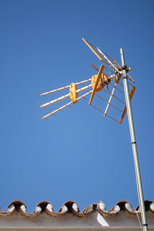 Television antenna on a typical roof against a clear blue sky, receiving and sending broadcasting signalsの写真素材