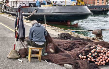old sailor repair fishing net in the harbour of la spezia