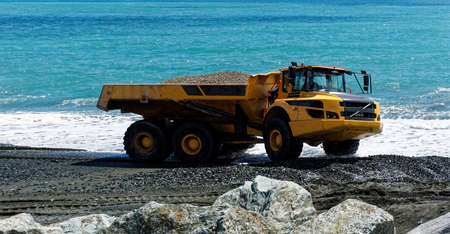 Industrial dumper trucks working on a construction in Genova city beach - Digging and moving sand with large dumper truck with sea in backgroundのeditorial素材