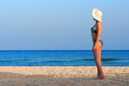 Sexy woman on the beach in a sunny day with blue sky and clear sand with white hatの写真素材