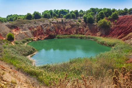 red soils around the freshwater lake formed in a former quarry for the extraction of bauxite in Italyの写真素材