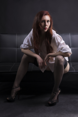Sexy red hair woman in lingerie on a black leather sofa looking rightの写真素材