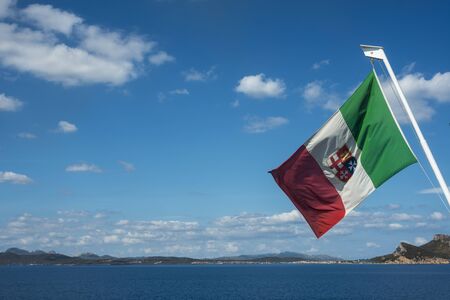 Seaside view of Golfo Aranci in morning light with Italian flag, Sardinia Italy