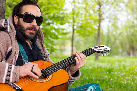 Hippy man with beard and glasses playing guitar outdoors on the grass