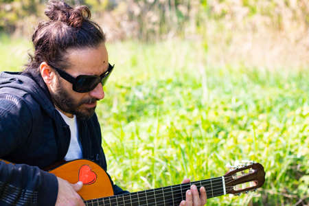 Hippy man with beard and glasses playing guitar outdoors on the grass