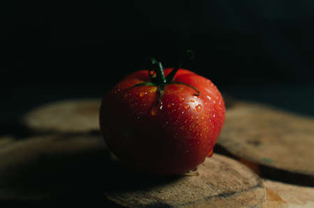 Red juicy and desirable tomato on a piece of wood on a black backgroundの写真素材