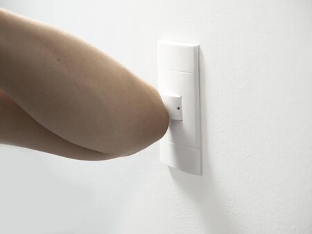 arm and elbow of person turning off and turning on power switch on white wall concept prevention of...