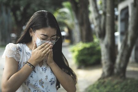 woman in outdoor room with head bowed eyes closed sneezing with masks putting her hands on her faceの写真素材