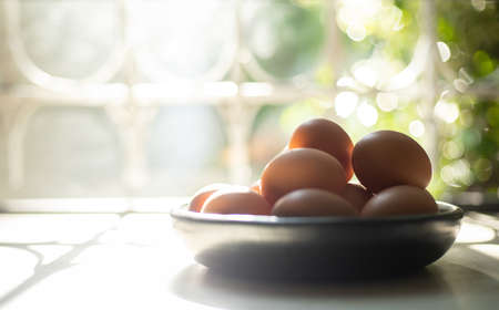 chicken eggs on a black plate on a wooden table with lights and shadows, coming in through the window.の写真素材