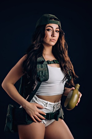 Sexy woman with military riot uniform in studio on dark background. A beautiful girl in short shorts...