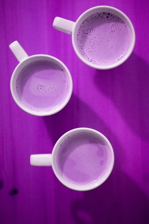 Purple abstract background with three white coffee cups, milk drink, top viewの写真素材