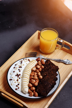 Healthy breakfast bowl and a glass of freshly squeezed orange juice on a wooden tray on a black background. Close upの写真素材