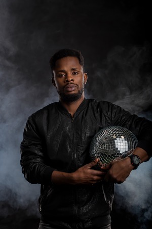 Confident brutal dark skinned man holding disco ball, looking at camera, going to party with...