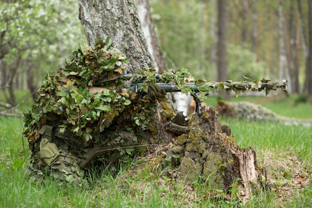 Camouflaged sniper in the forest in ambush. Military man aiming a gun, a rifle at the enemy in natureの写真素材