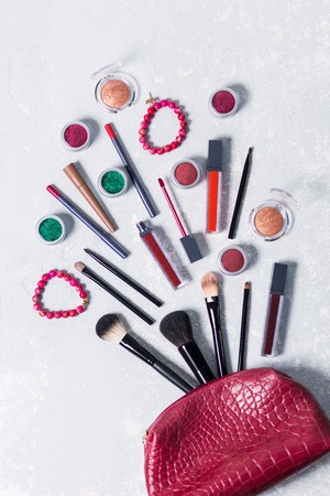 Fashion accessories. Makeup collection. Female trendy red cosmetic bag, professional cosmetics goes red purse on a white light background, brush, lipstick, shadow eyeshadow, pencils, braceletsの写真素材